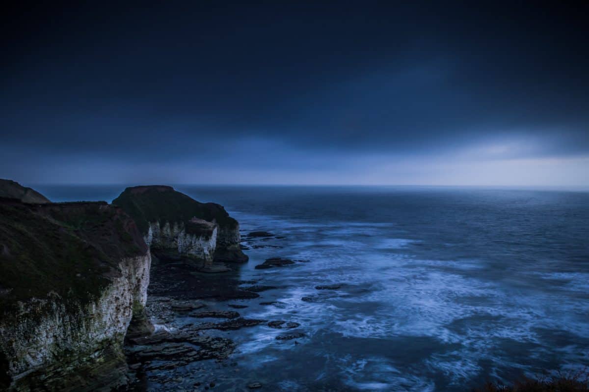 Beach with overhanging cliff at night.